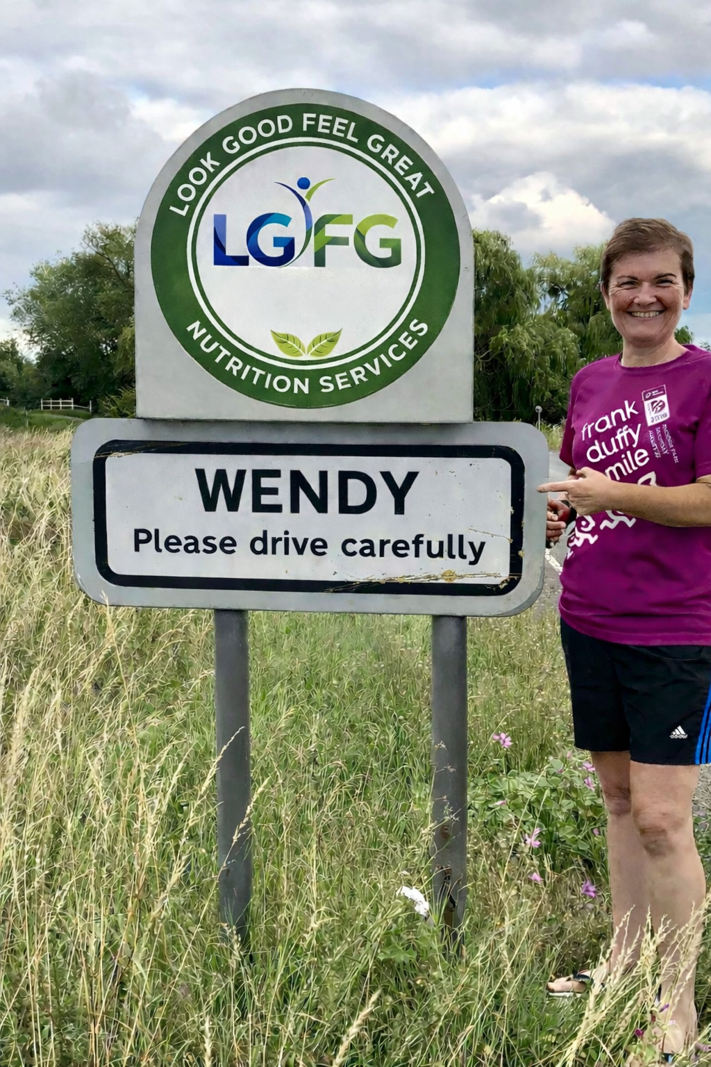 Picture of Wendy standing next to Wendy village sign with her logo superimposed on to the speed limit sign