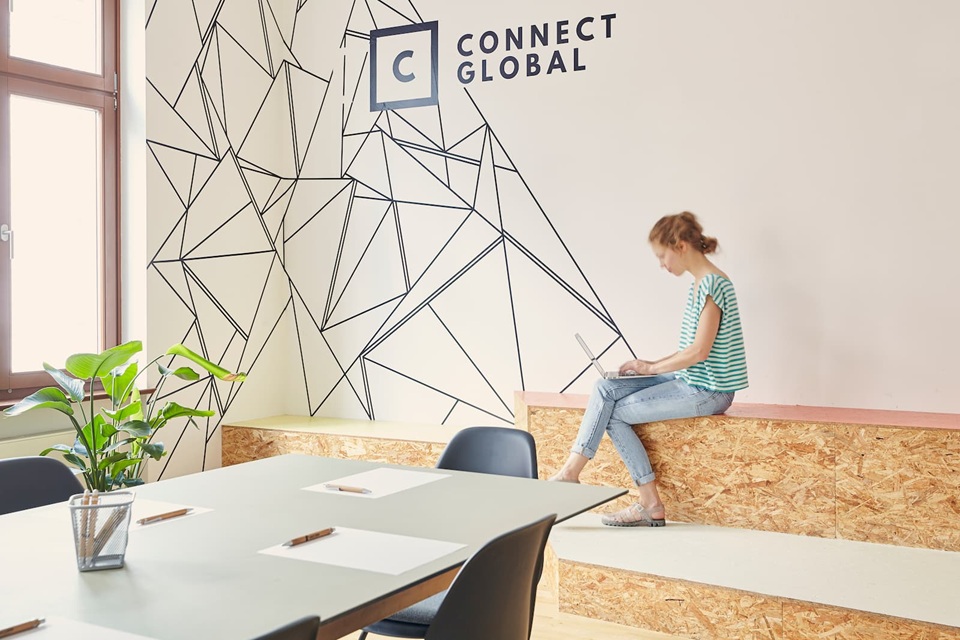 Kollaborative Arbeitsplätze in Hamburg – Kreatives Bürodesign für moderne Teams Moderne Arbeitsumgebung mit kreativem Wanddesign, flexiblen Sitzbereichen und junger Mitarbeiterin am Laptop im Büro von Connect Global in Hamburg.