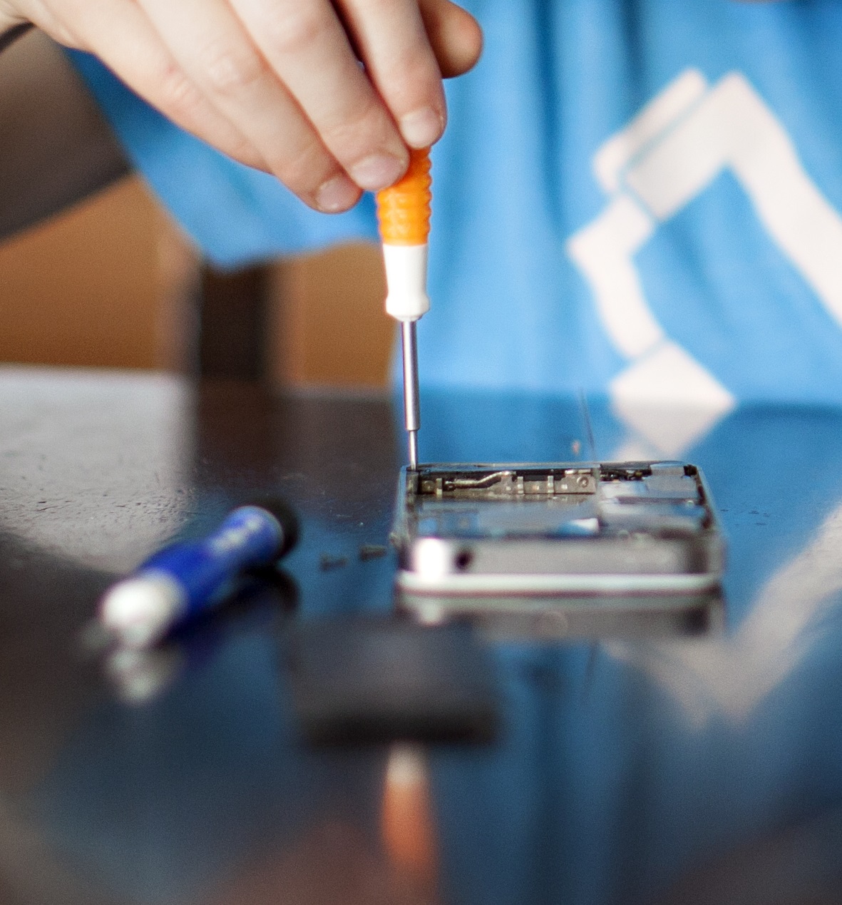 chopiec w niebieskiej koszulce naprawia telefon komórkowy typu smartfon za pomocą śrubokrętów
